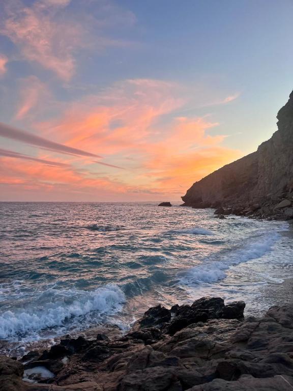 a sunset over the ocean with rocks in the water at Pequeño estudio frente al mar, piscina y parking in Villajoyosa
