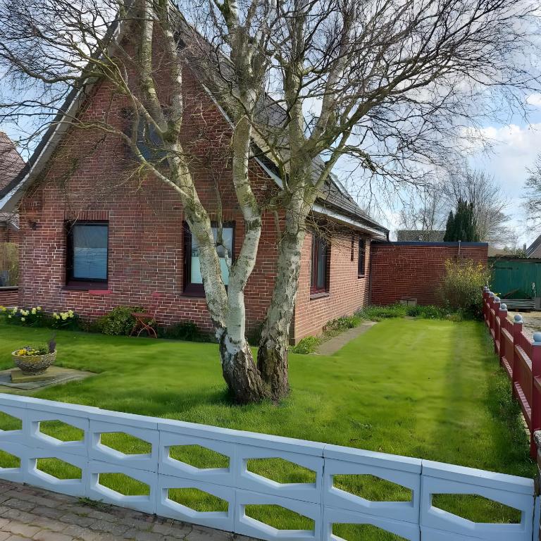 a white fence in front of a house with a tree at Ferienhaus Hadler in Kaiser Wilhelm Koog