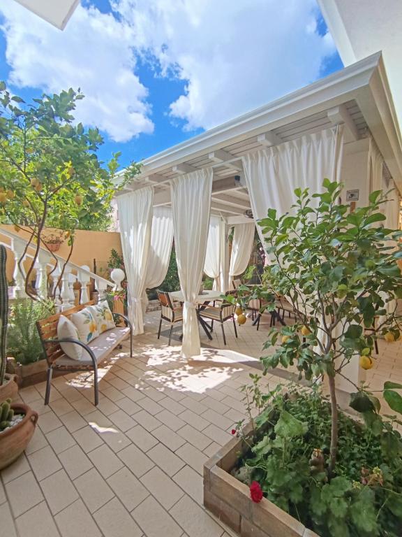 a patio with white curtains and a table and chairs at Domos Le Due Tuie in Piscinas