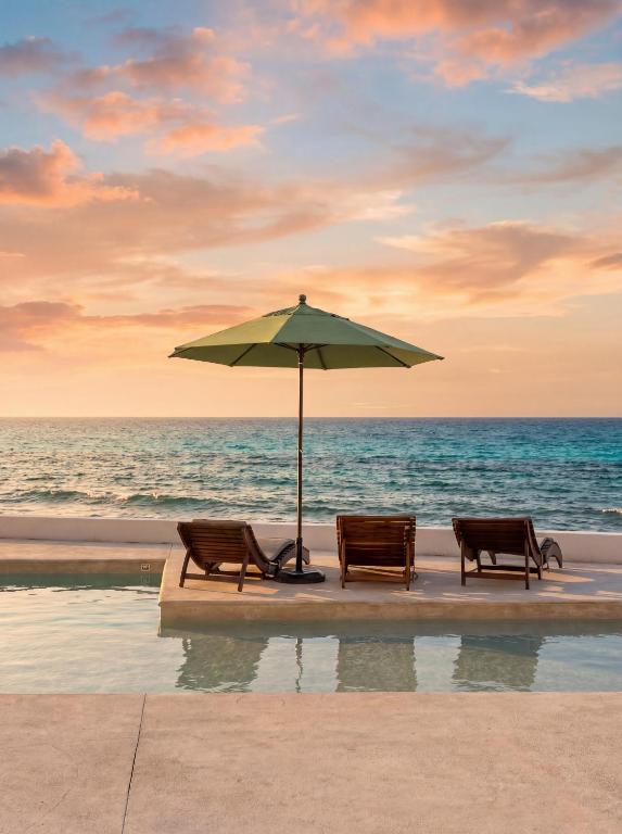three chairs and an umbrella on the beach at Playa Norte Oceanfront Remote Work Plus Concierge in Isla Mujeres