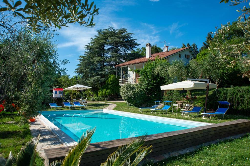a swimming pool in the yard of a house with chairs and umbrellas at Villa Cassiani in Fiorenzuola di Focara