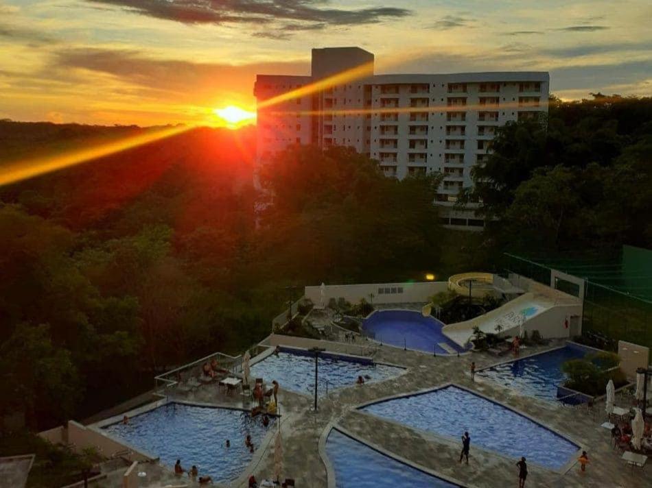 a sunset over two swimming pools in a city at Flat Aconchegante - Park Veredas 417 in Rio Quente