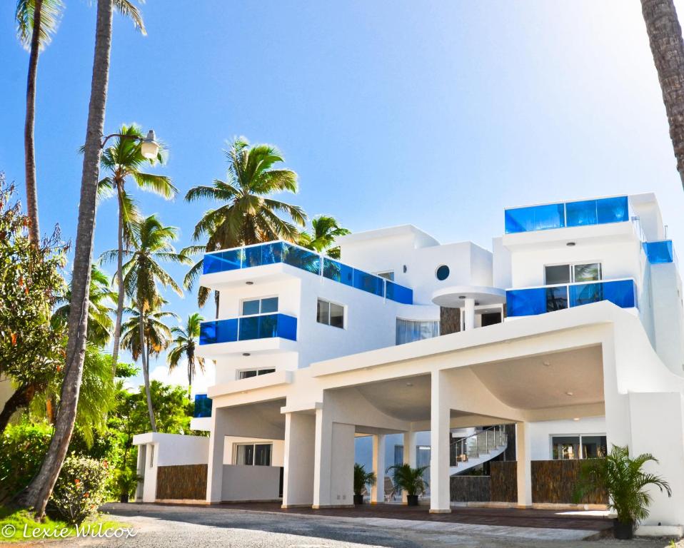 un edificio blanco con balcones azules y palmeras en The Sanctuary @ Los Corales en Punta Cana