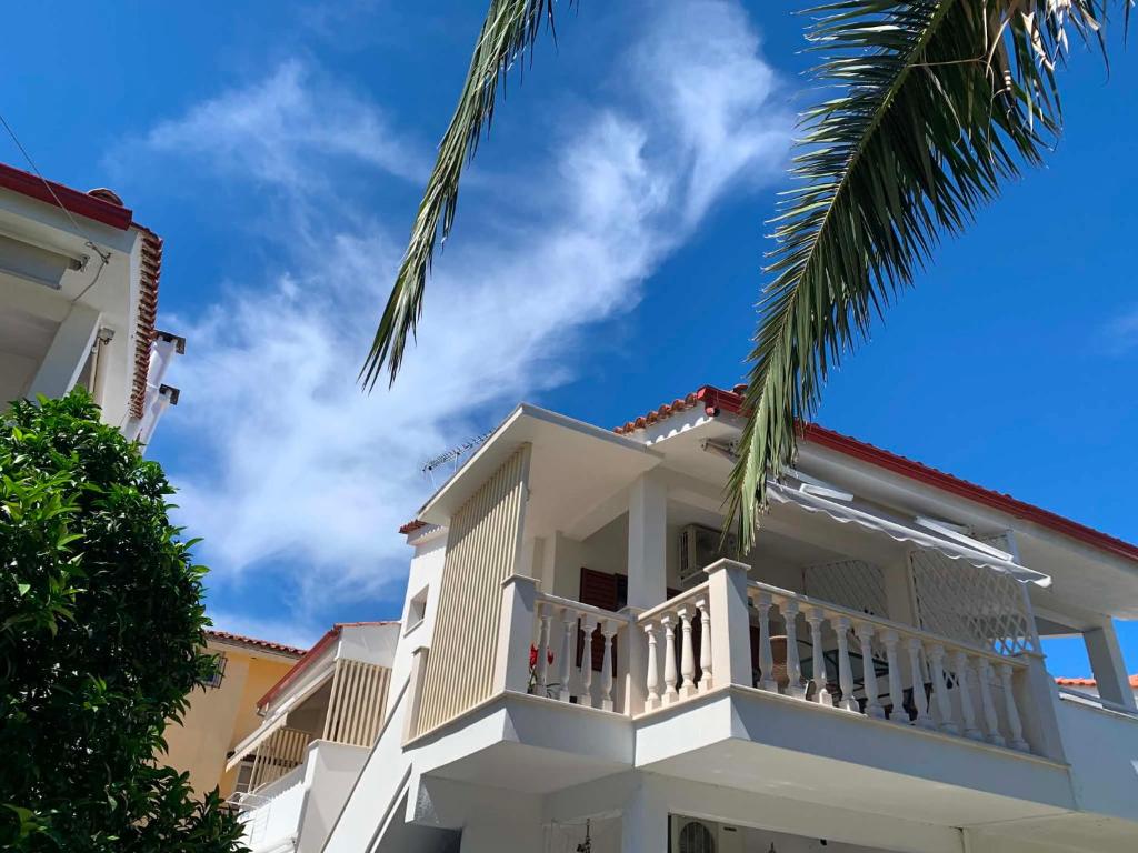 a white house with a balcony and a palm tree at Miminllari APARTMENTS 2 in Pefkochori