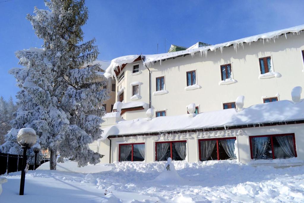 un edificio cubierto de nieve frente a un árbol en Hotel Victoria, en Rivisondoli