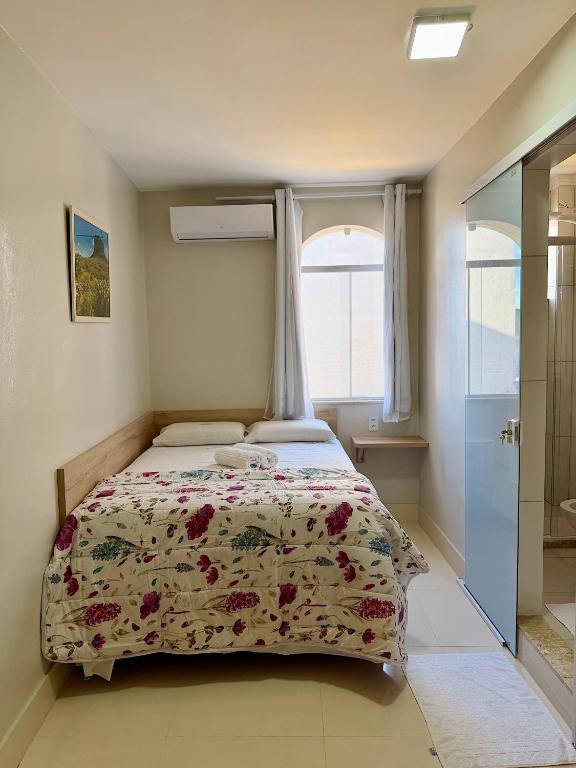 a bedroom with a bed with a floral bedspread and a window at Hotel C Diamantina in Vitória da Conquista