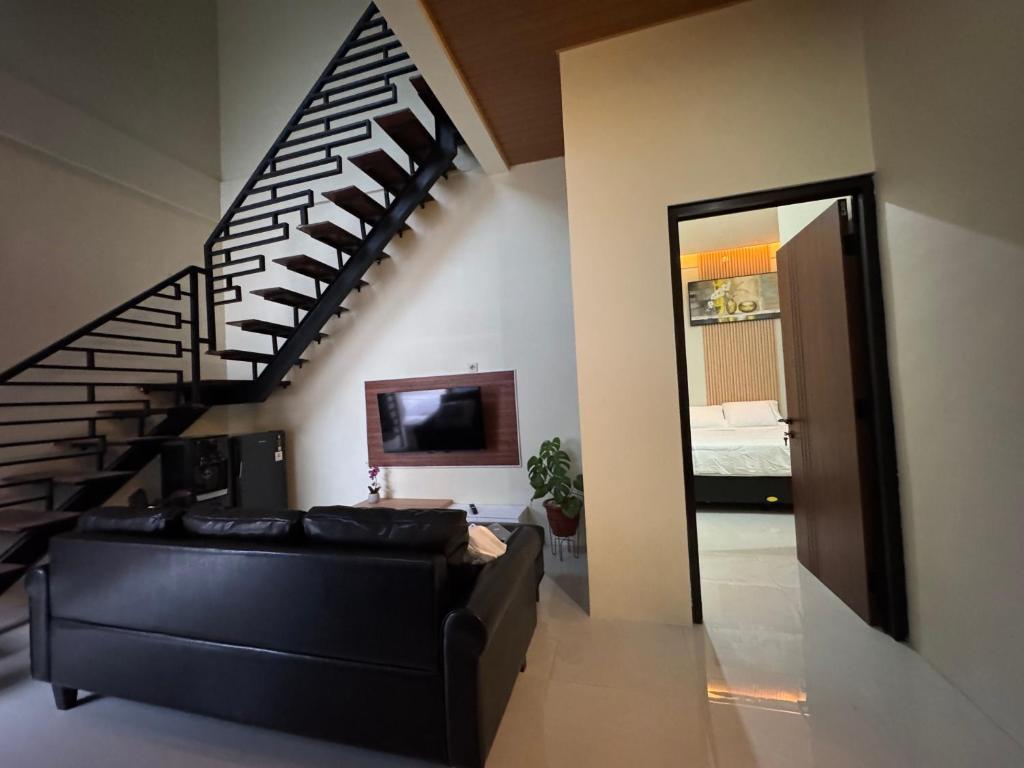 a living room with a black couch and a staircase at Omah Tentrem Magelang in Magelang