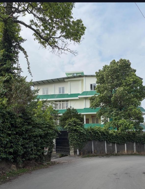 a white building with trees in front of it at Apsara Guest House, Peaceful Area in Central Shillong in Shillong