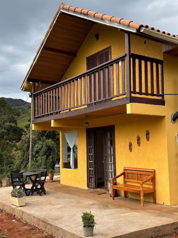 a yellow house with a balcony and a bench at Chalé Recanto da Grota in Passa Vinte