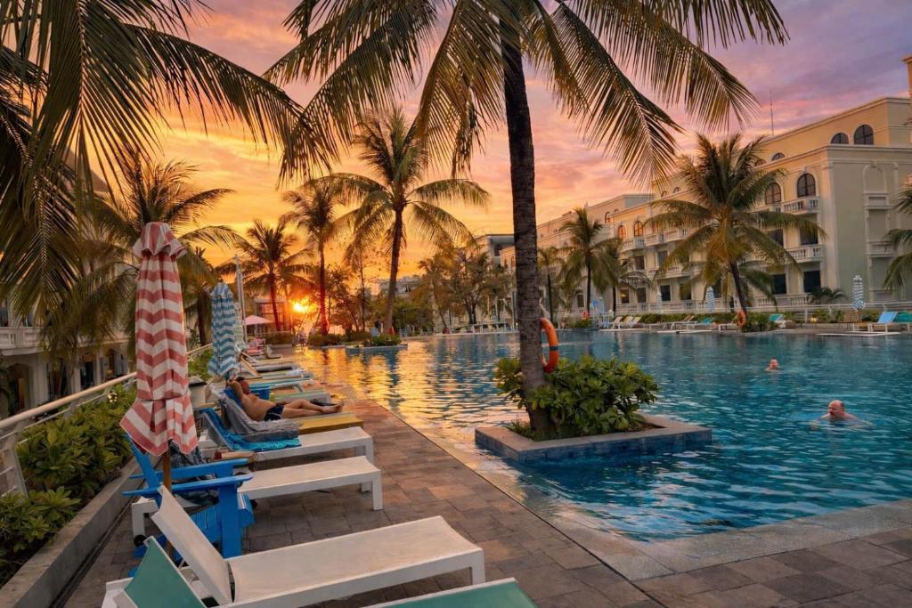 a pool at a resort with palm trees and lounge chairs at LALU Hotel in Phú Quốc