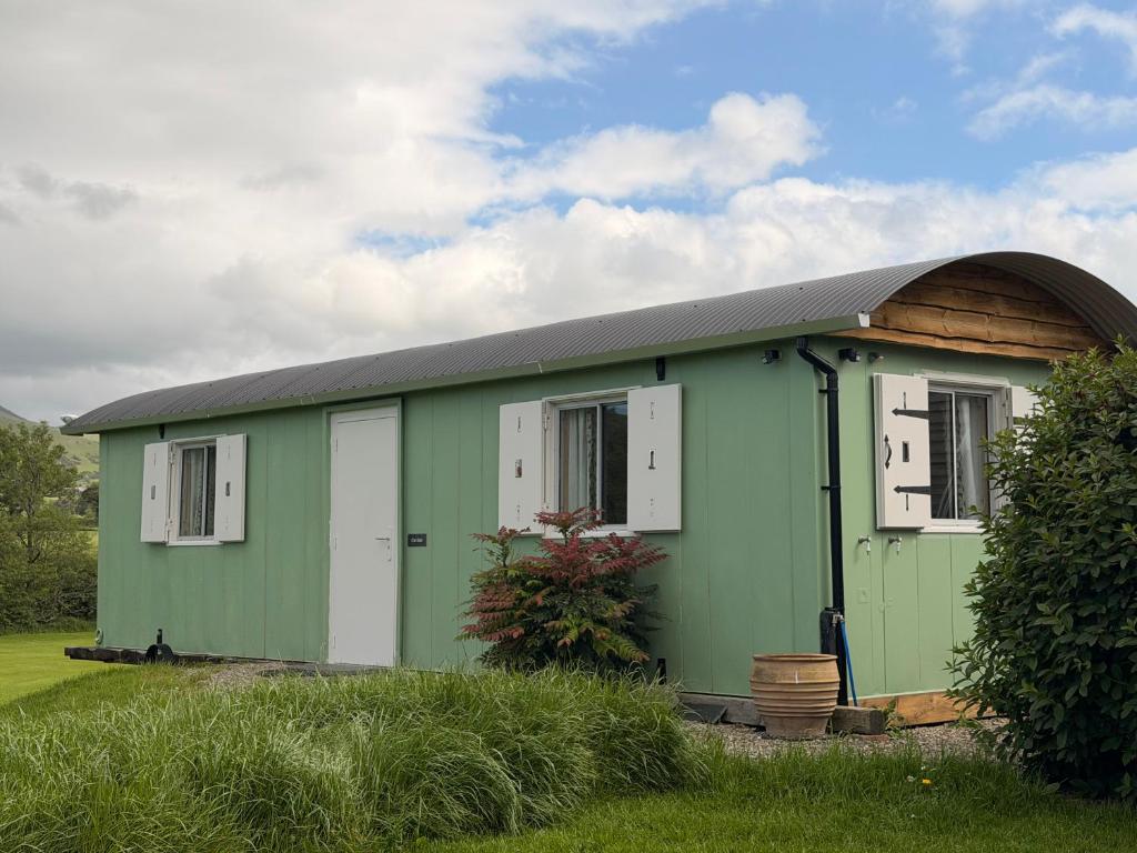 a green building with a gambrel roof and windows at Cwt Ieir in Ruthin