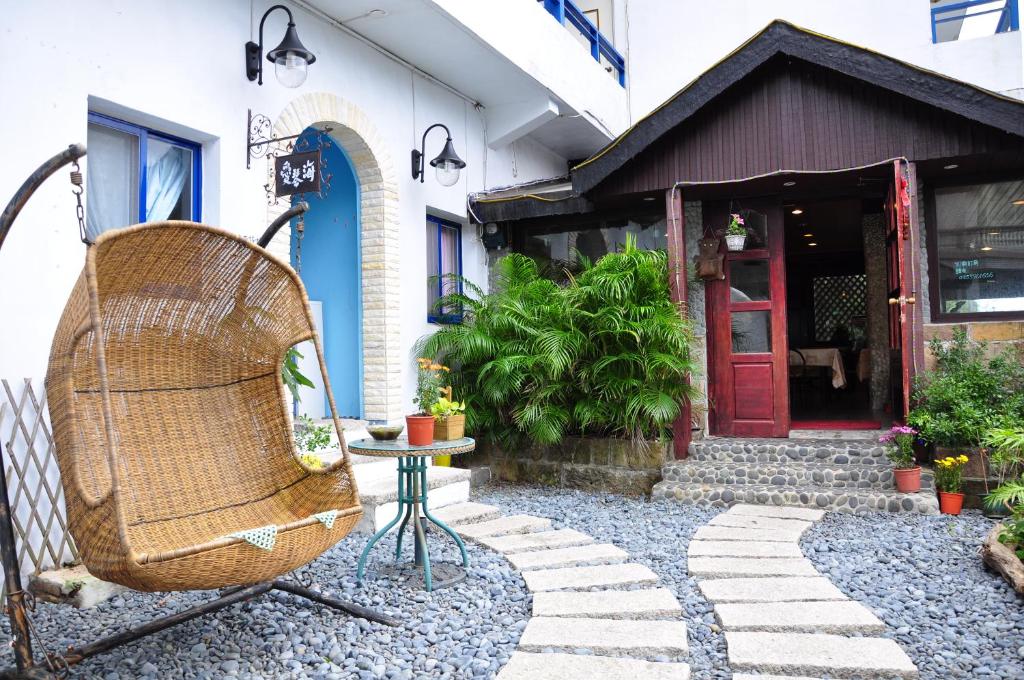 uma cadeira de vime sentada do lado de fora de uma casa com uma porta vermelha em Aegean Sea Guest House em Jiufen