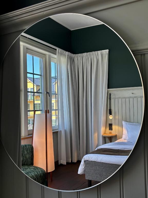 a mirror reflecting a bedroom with a bed and a window at Lilla Hotellet Blidö in Blidö