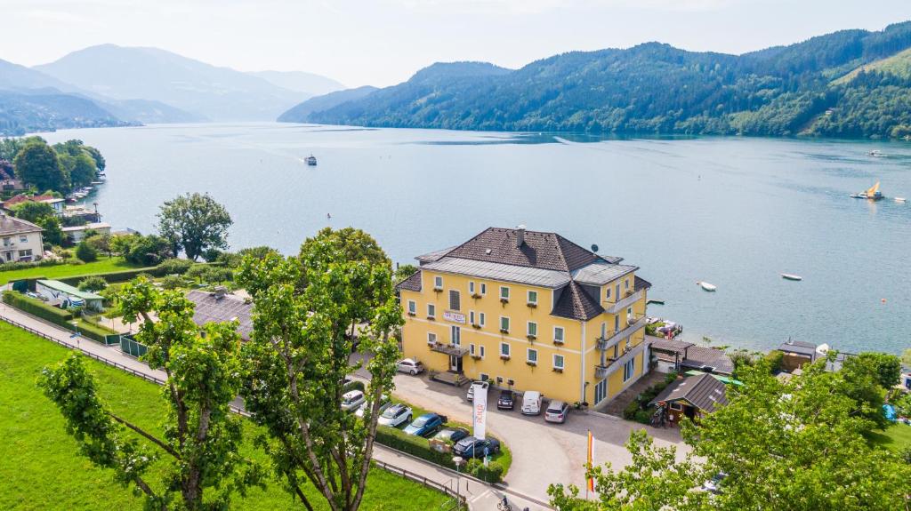 a large yellow building on the shore of a lake at Strandhotel Pichler in Seeboden