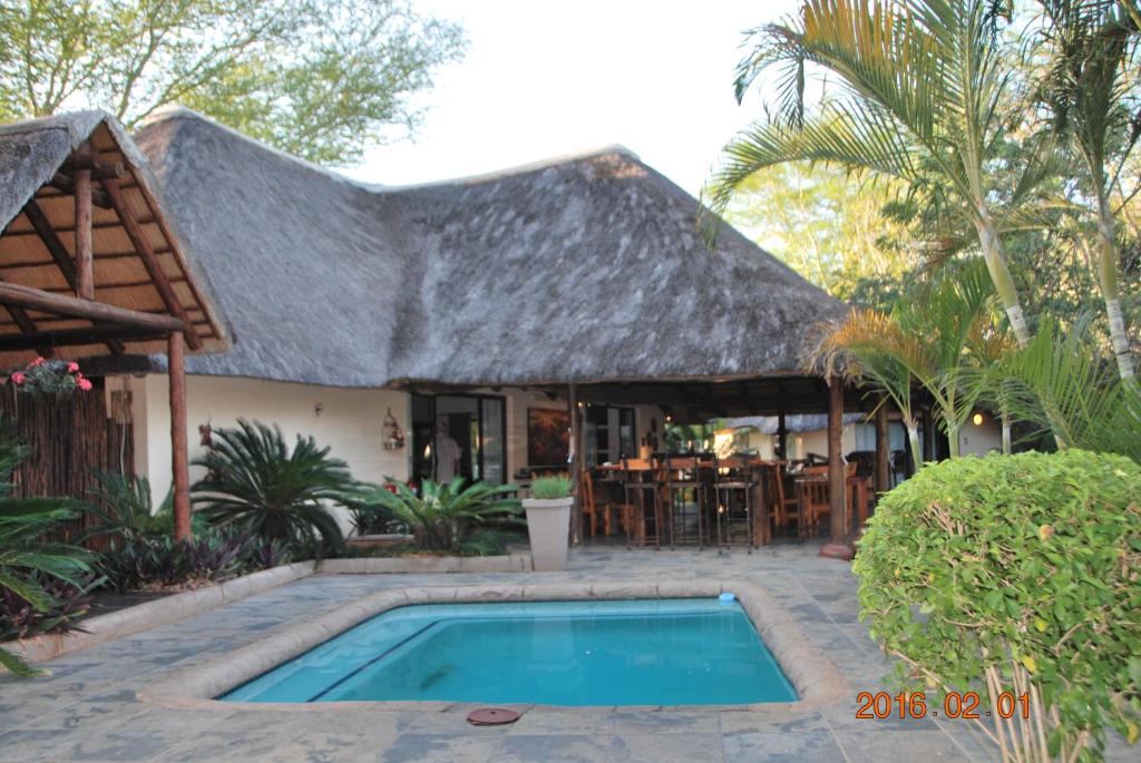 uma casa com telhado de palha e uma piscina em Acasia Guest Lodge em Komatipoort