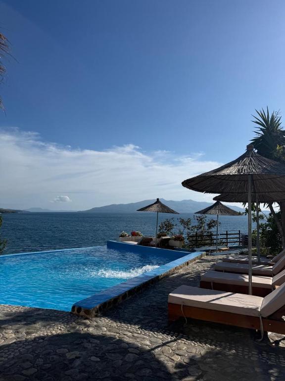a swimming pool with chairs and umbrellas next to the ocean at Apartments Romario in Sarandë