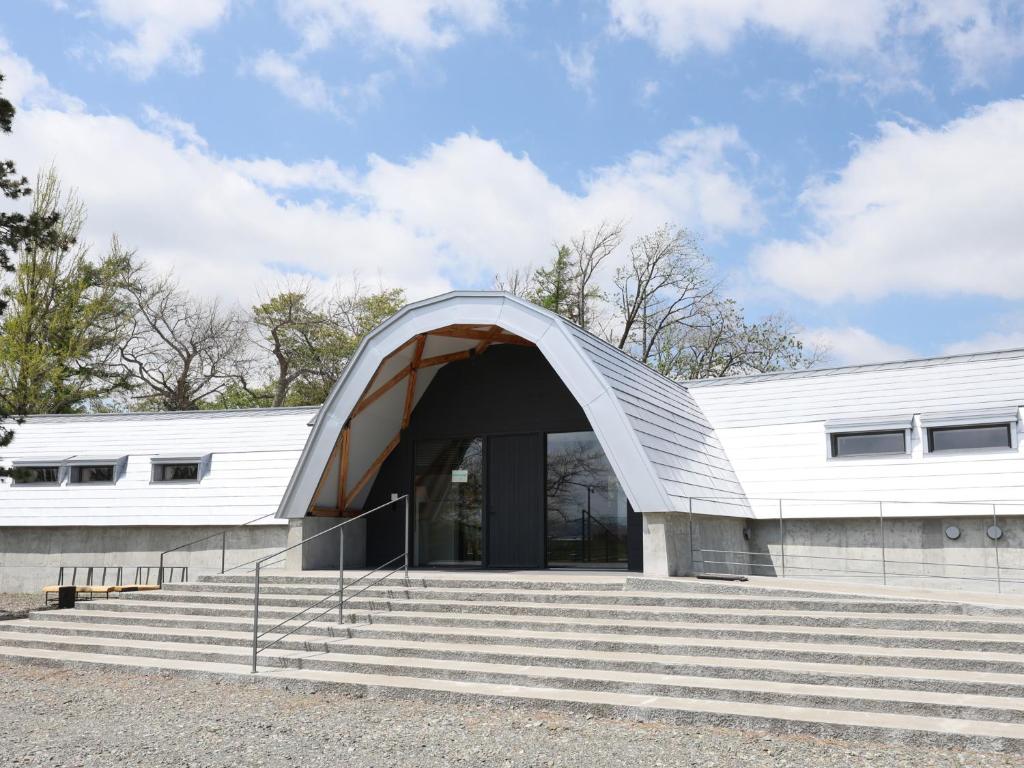 a white building with a curved roof and stairs at 友愛ファームゲストハウス in Hatoyama