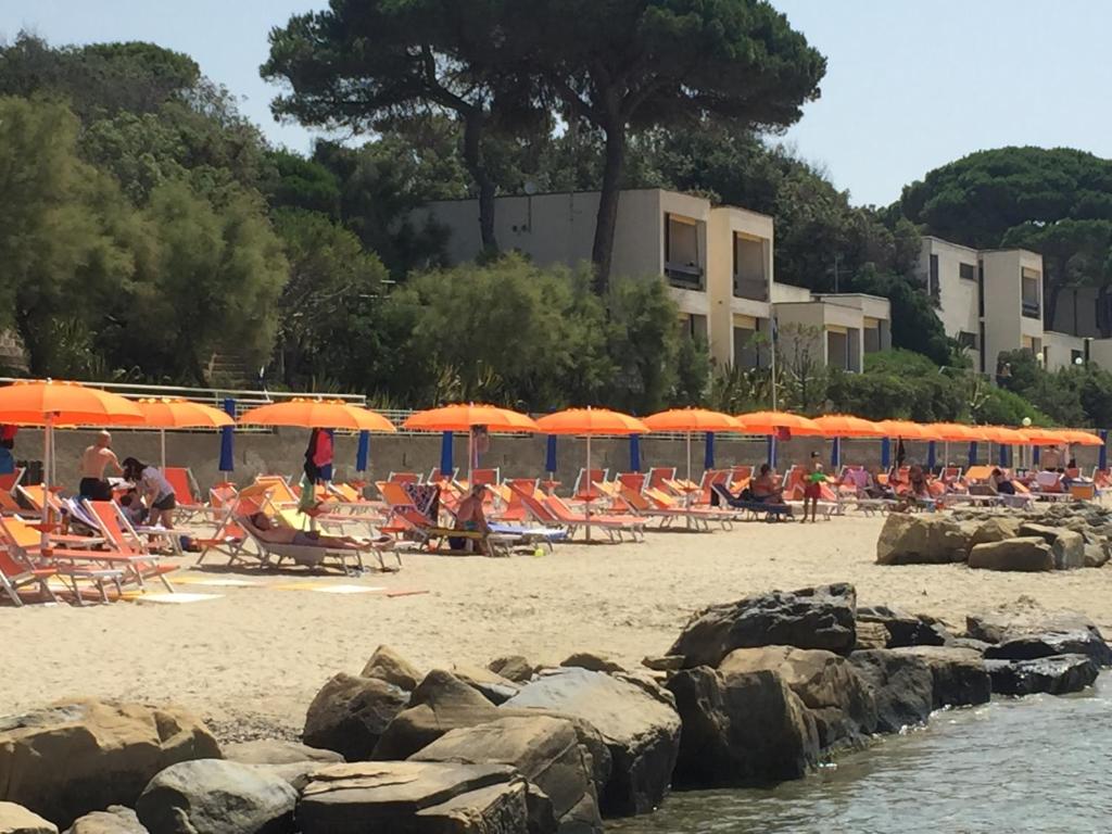 ピオンビーノにあるBaia Toscanaの多くの椅子とオレンジのパラソルが備わるビーチ