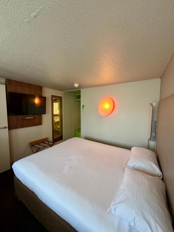 a bedroom with a large white bed with a light on the wall at Campanile Chambéry in Chambéry