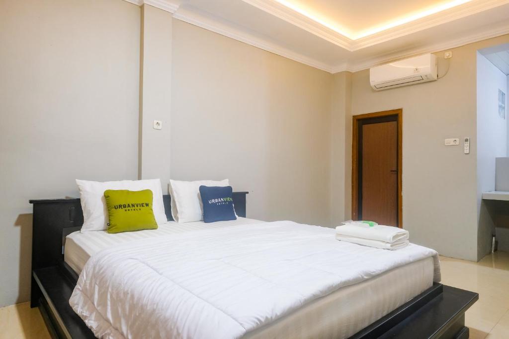 a bedroom with a large white bed with yellow and blue pillows at Urbanview TWH Costel near Stadion Maguwoharjo Yogyakarta in Yogyakarta