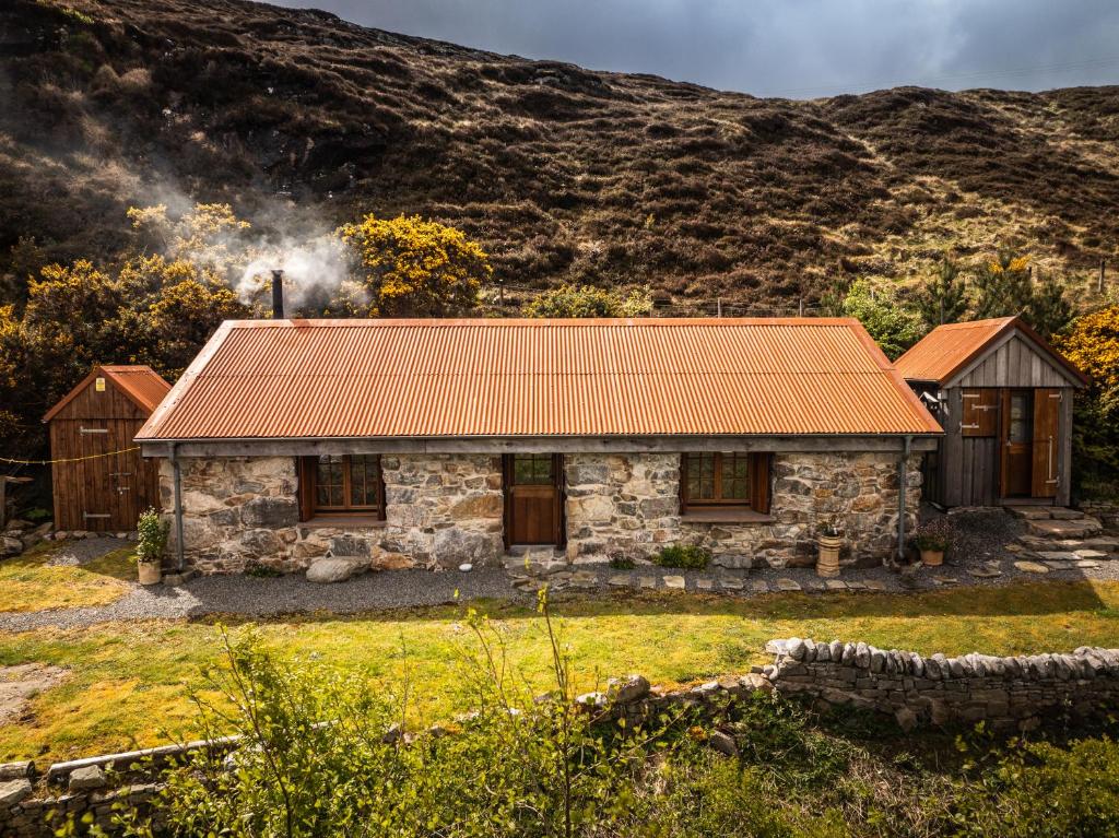 a stone house with an orange roof in front of a mountain at Mullach Dearg in Tarbert