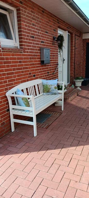 a white bench sitting on the side of a brick house at Ferienwohnung am Wind mit Dachterasse in Bredstedt