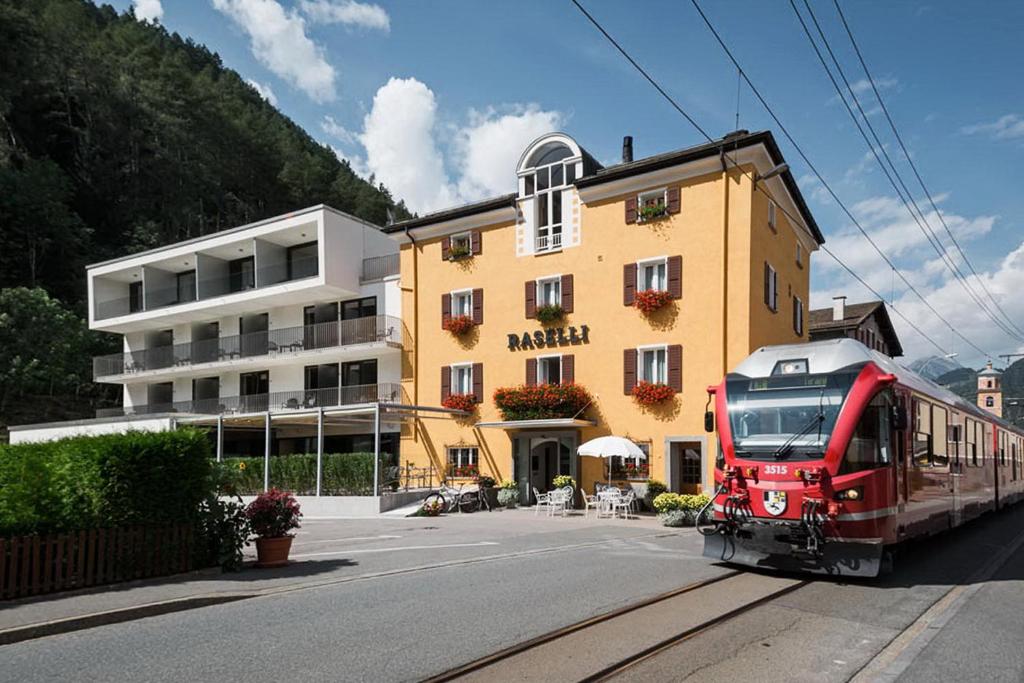 Un treno rosso passa davanti a un edificio di Raselli Sport Hotel a Poschiavo