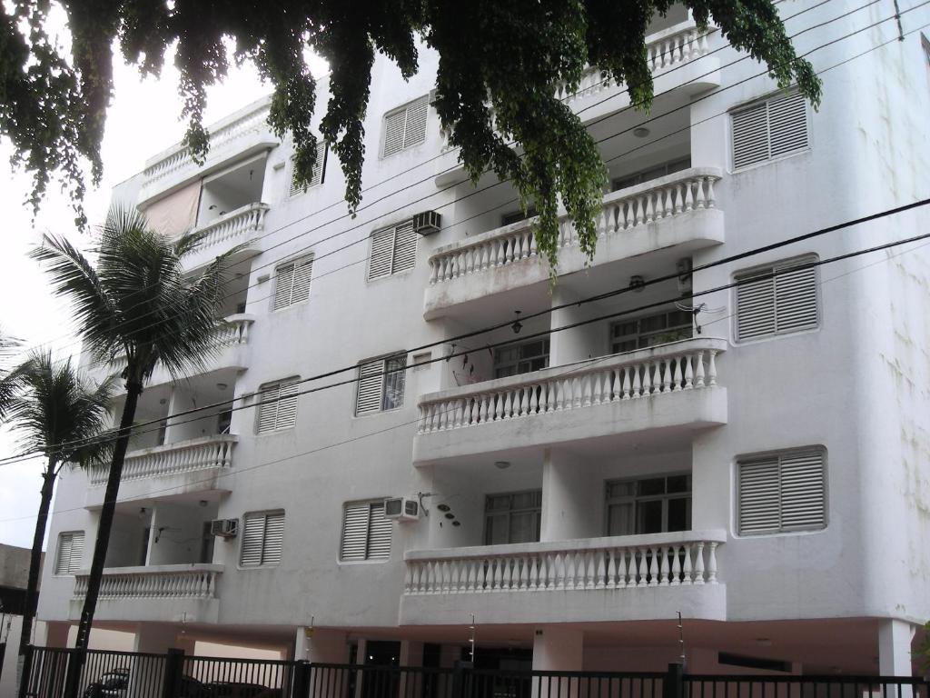 a white building with balconies and a palm tree at Condominio Edifício Las Vegas in Guarujá