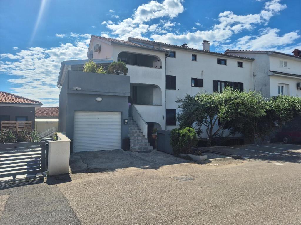 a white house with a garage in a parking lot at Apartment Vdovjak in Malinska