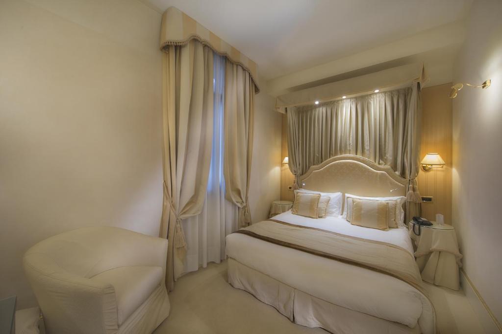 a white bedroom with a bed and a chair at Hotel A La Commedia in Venice