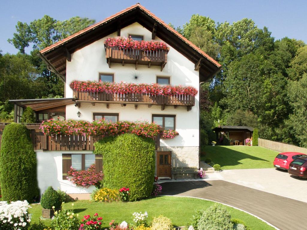 ein weißes Haus mit roten Blumen und einem Balkon in der Unterkunft Ferienwohnungen Göstl in Bodenmais