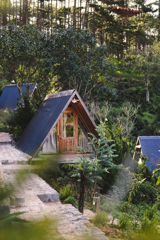 a small cabin with a black roof in a forest at À La Main Farmhouse in Ấp Trường Sơn