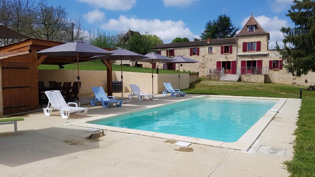 a swimming pool with chairs and umbrellas next to a house at La truffière in Belvès