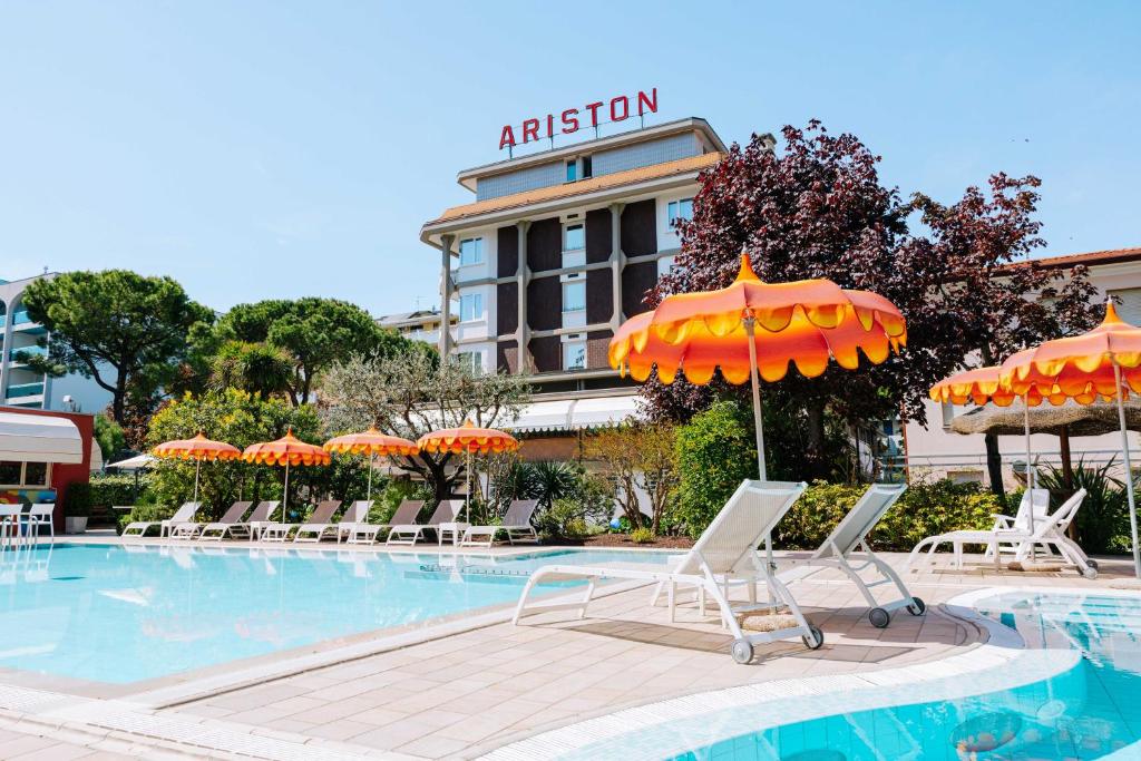 a pool with chairs and umbrellas in front of a hotel at Hotel Ariston in Bibione