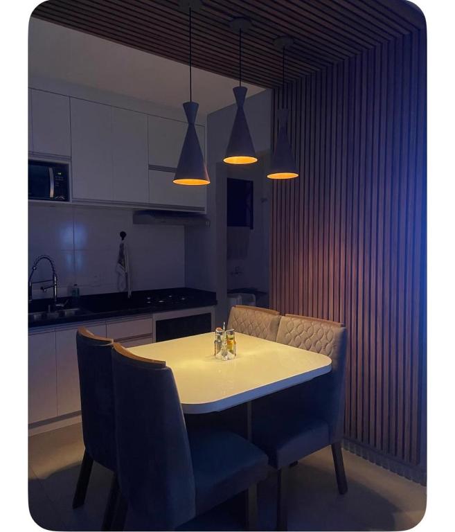 a kitchen with a white table with chairs and lights at Apartamento Tranquilo e Aconchegante in Carmo do Rio Claro