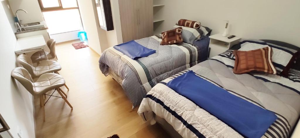 a bedroom with two beds and a chair and a table at Edificio Paradisíaco,Cochabamba in Cochabamba