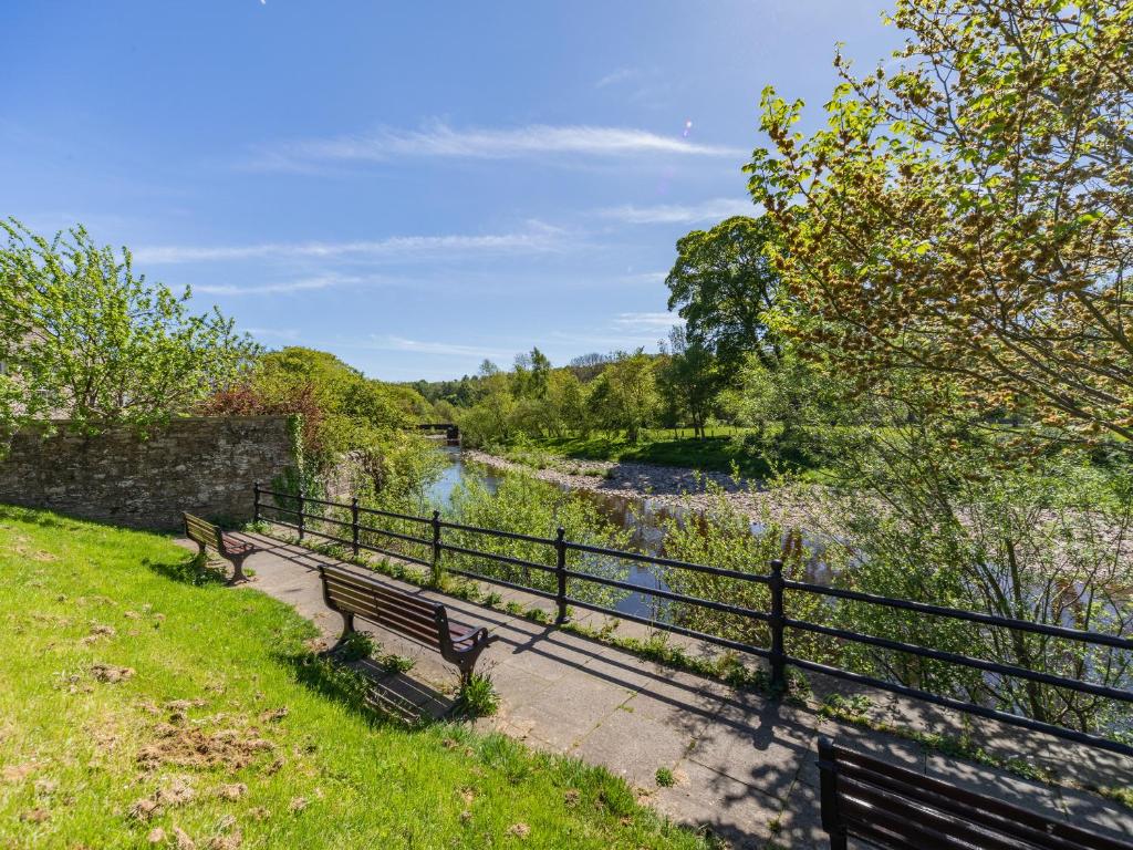 two benches sitting next to a fence next to a river at Squirrel Cottage - Uk37886 in Stanhope