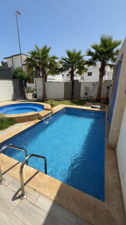 two swimming pools with palm trees in front of a building at Villa Piscine Jacuzzi Saïdia 3 chambres in Saïdia
