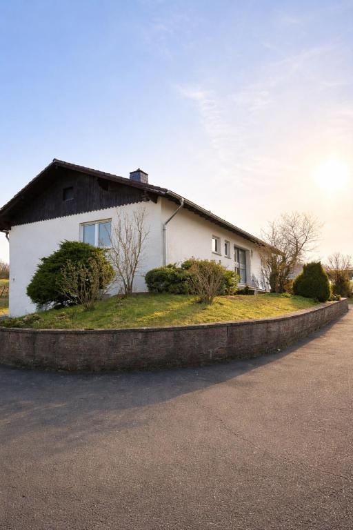 Haus Eifelkind في Basberg: بيت أبيض مع شجيرات وأشجار أمامه