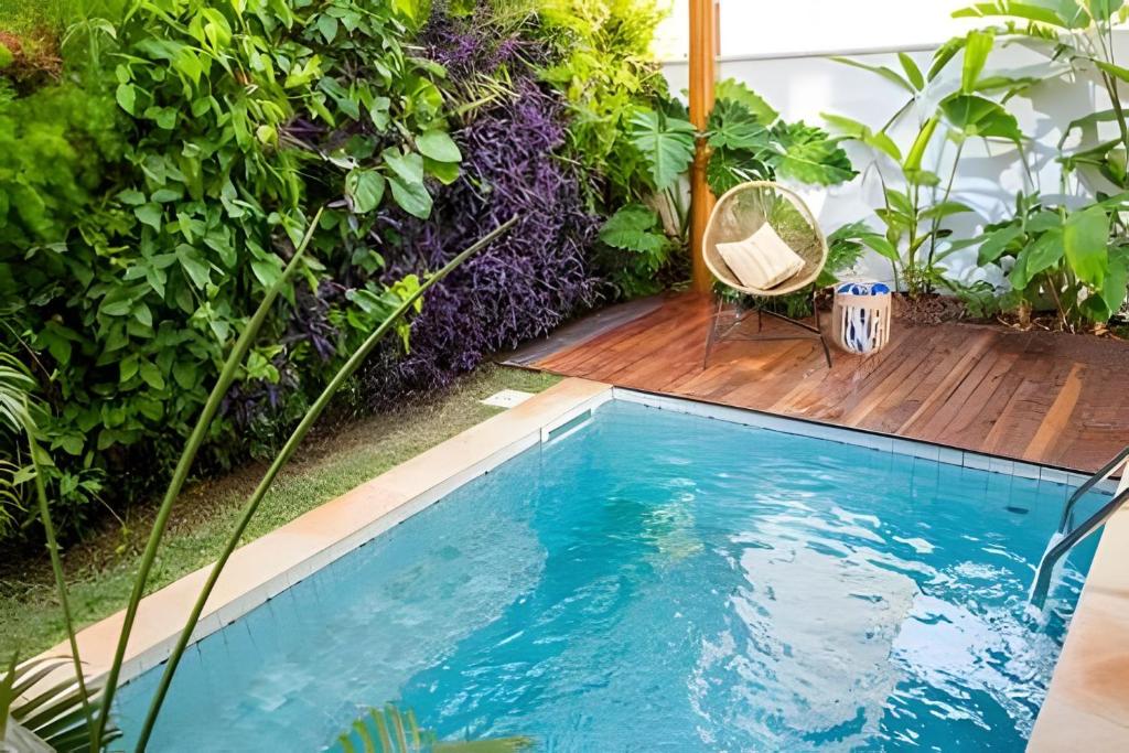 a swimming pool in a garden with a chair next to it at Refugio de Luxo com Piscina e Jacuzzi em Pipa in Pipa