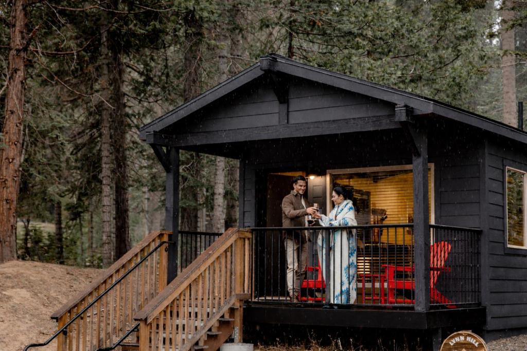 a man and woman standing on the porch of a black cabin at Waybound Yosemite in Fish Camp