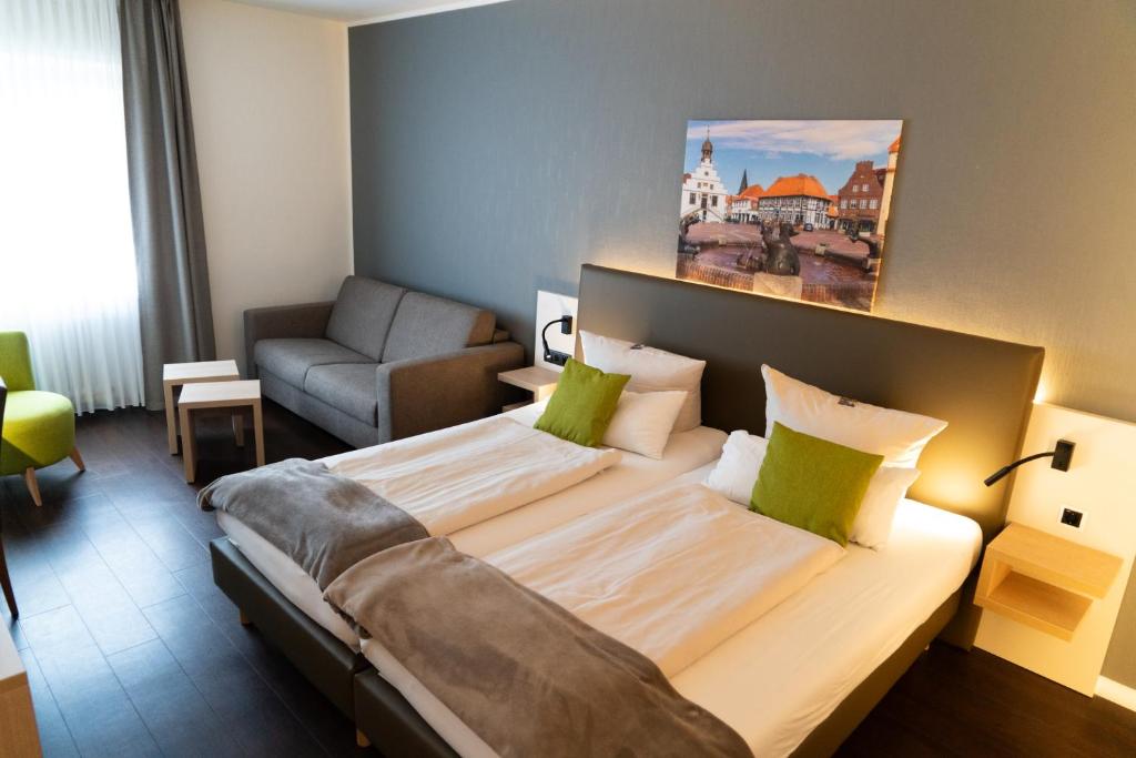 a bedroom with a large bed with a couch and a chair at Stadthotel im Kolpinghaus Lingen in Lingen