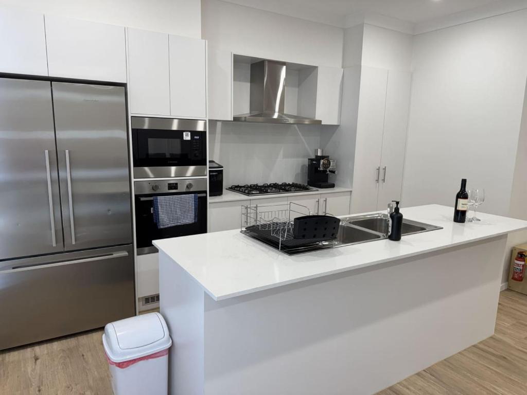 a kitchen with white cabinets and a stainless steel refrigerator at Spacious New Home for 12 Guests in Campbelltown South