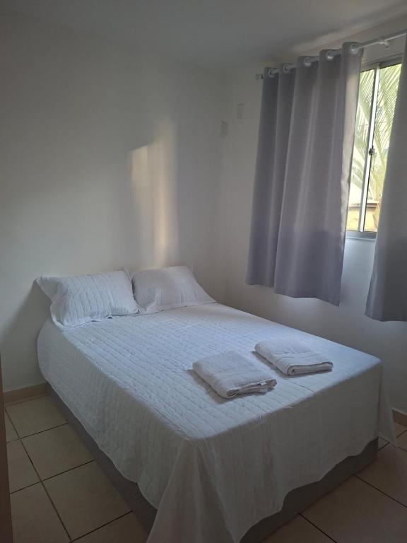 a white bedroom with a bed with towels on it at Apto completo térreo 2quartos - praia e shopping in Rio das Ostras