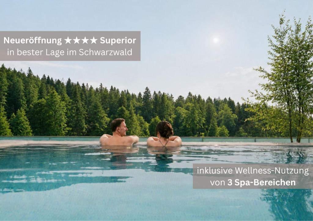 two people swimming in a pool of water at Das Waldhotel - Spa & Wellness Resort in Todtnau