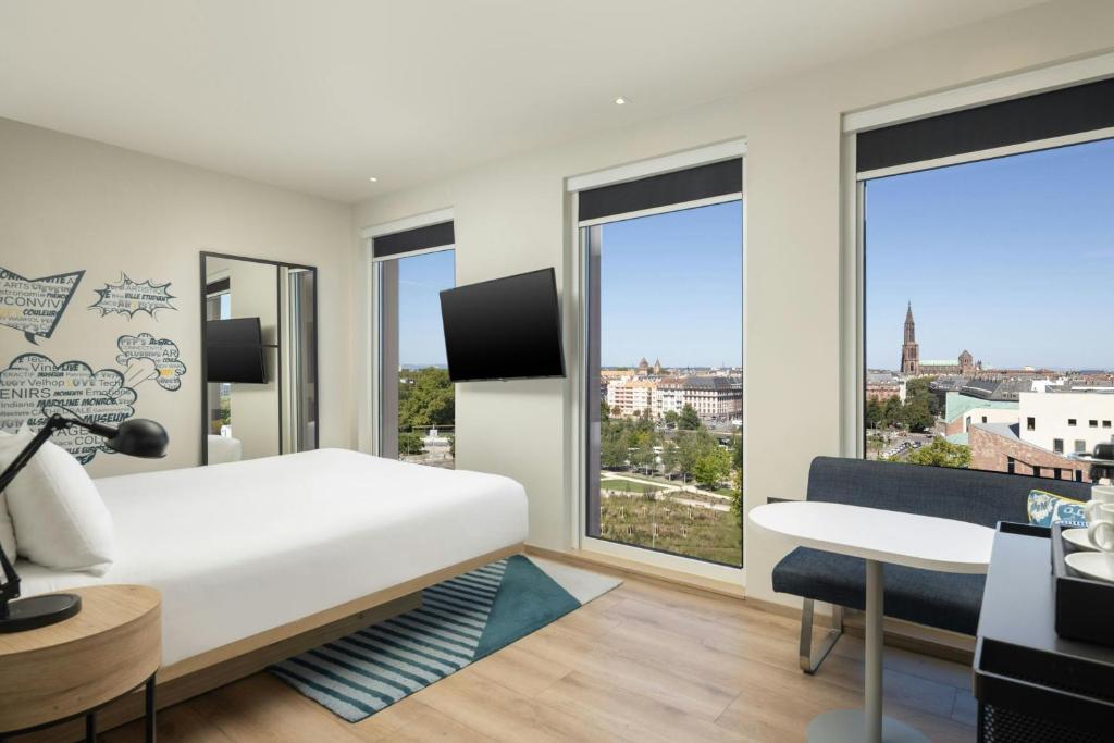 a bedroom with a bed and a desk and windows at Aloft by Marriott Strasbourg City Centre in Strasbourg