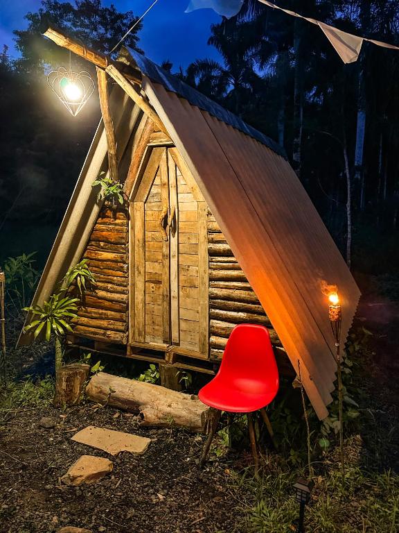 a red chair sitting in front of a small cabin at Chalé Moon - Vale do ribeira in Juquiá