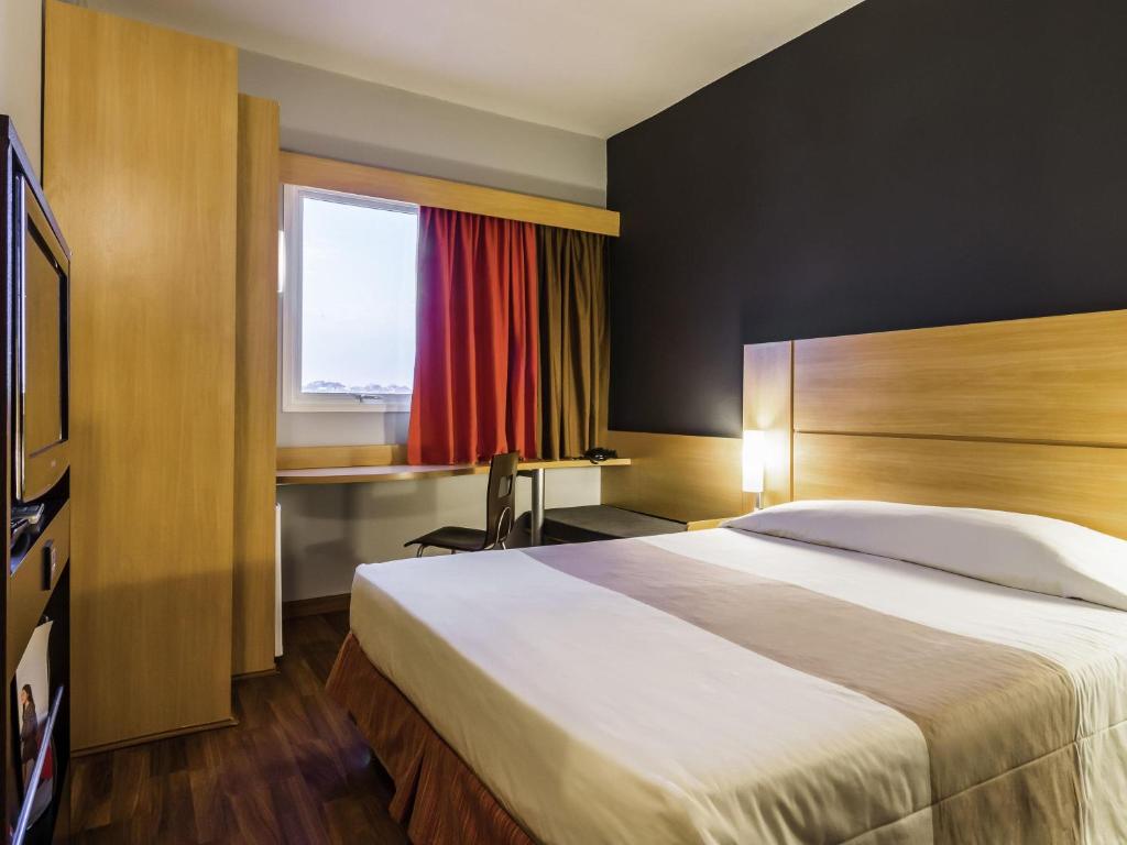 a hotel room with a bed and a desk and a window at ibis Jaboticabal in Jabuticabal