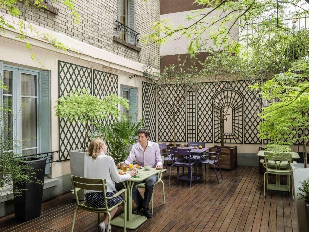 a man and woman sitting at a table on a patio at Aparthotel Adagio Access Paris Philippe Auguste in Paris