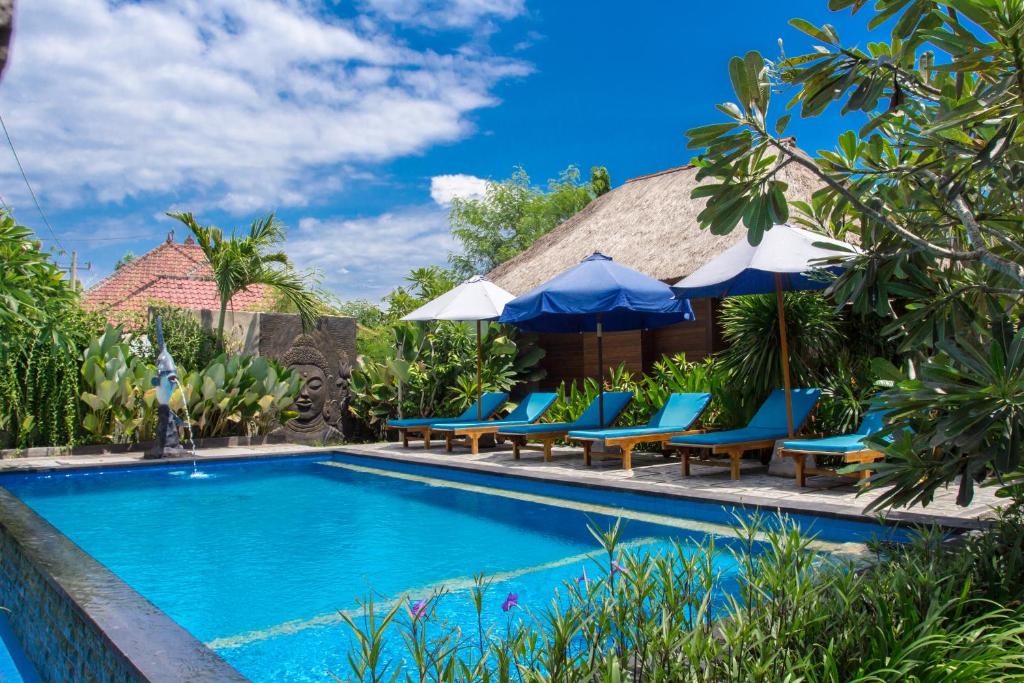 a pool at a resort with blue chairs and umbrellas at Koji Garden Huts - CHSE Certified in Nusa Lembongan